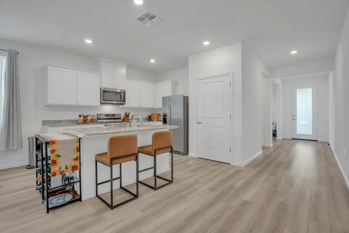 kitchen with a breakfast bar, light stone countertops, white cabinetry, stainless steel appliances, and light wood-type flooring