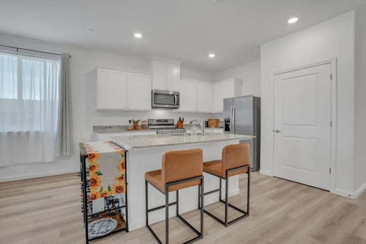 kitchen featuring light stone countertops, white cabinets, stainless steel appliances, a breakfast bar area, and a kitchen island with sink