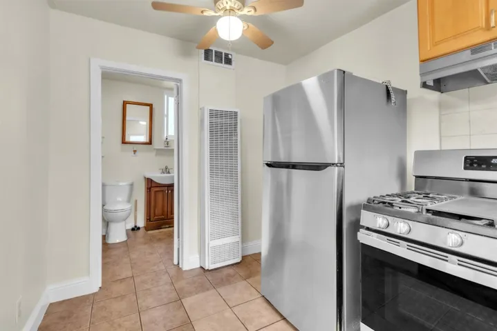 Kitchen with stainless steel appliances, range hood, light tile patterned floors, a heating unit, and a ceiling fan