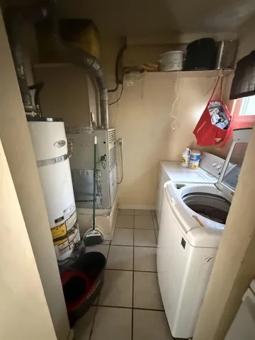Laundry area with light tile patterned floors, strapped water heater, heating unit, and washer and clothes dryer