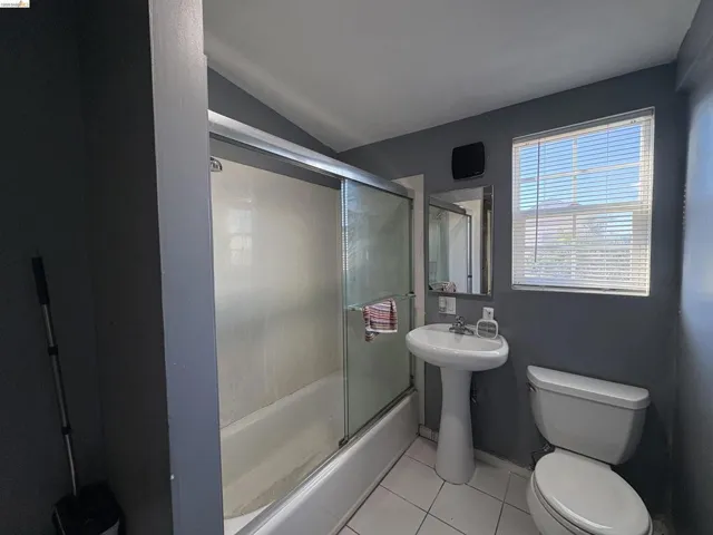 Full bathroom featuring light tile patterned floors, bath / shower combo with glass door, and lofted ceiling