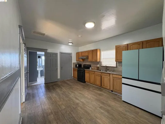 Kitchen with freestanding refrigerator, wood finish cabinetry, black gas range oven, dark wood finished floors, and tasteful backsplash