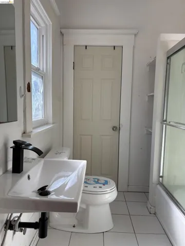 Full bath with combined bath / shower with glass door and light tile patterned flooring