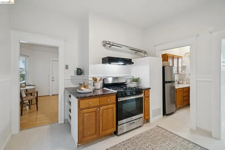 Kitchen with stainless steel appliances, wood finish cabinets, exhaust hood, dark stone counters, and wainscoting
