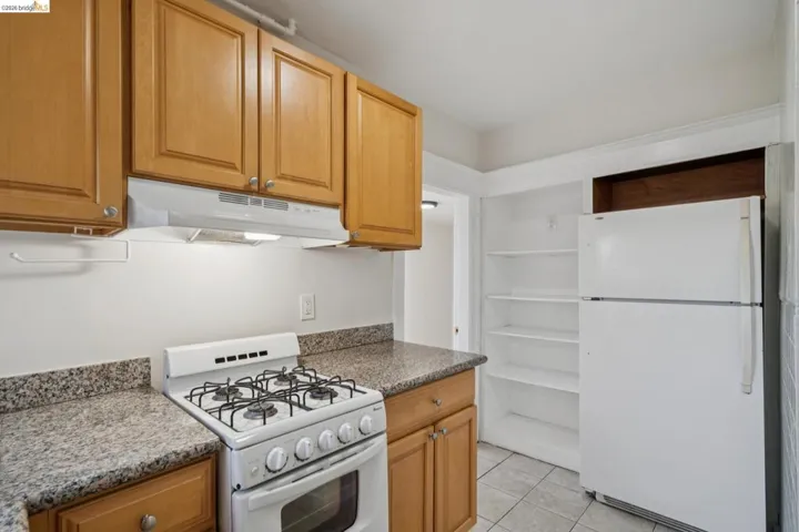 Kitchen with white appliances, light tile patterned flooring, dark stone countertops, and wood finish cabinetry