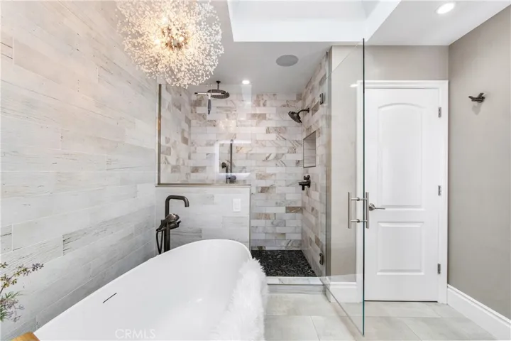 Luxurious spa bath featuring a sculptural soaking tub, marble shower, illuminated vanities, designer lighting, and custom closet.