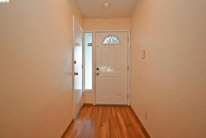 Doorway to outside with a textured wall, wood finished floors, and a textured ceiling