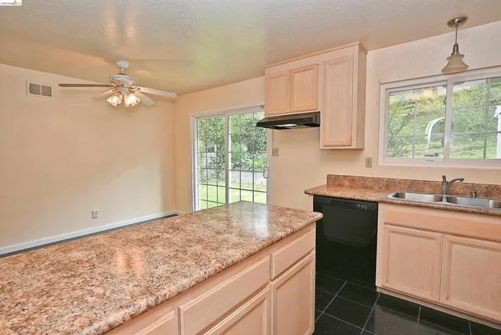 Kitchen with light wood finish cabinetry, black dishwasher, dark tile patterned floors, a ceiling fan, and decorative light​​‌​​​​‌​​‌‌​​‌​​​‌‌​​​‌​​‌‌​​‌‌​​‌‌​​​​ fixtures