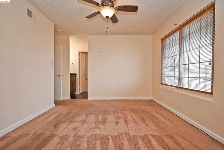 Empty room with a ceiling fan, light colored carpet, and a textured ceiling