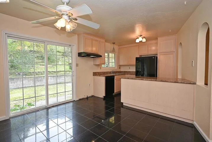 Kitchen featuring light wood finish cabinets, black appliances, dark stone counters, ceiling fan, and a peninsula