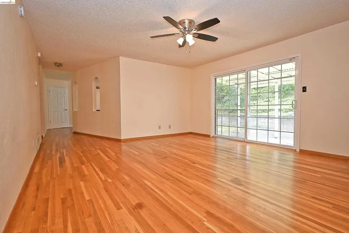 Empty room with ceiling fan, light wood-type flooring, and a textured ceiling