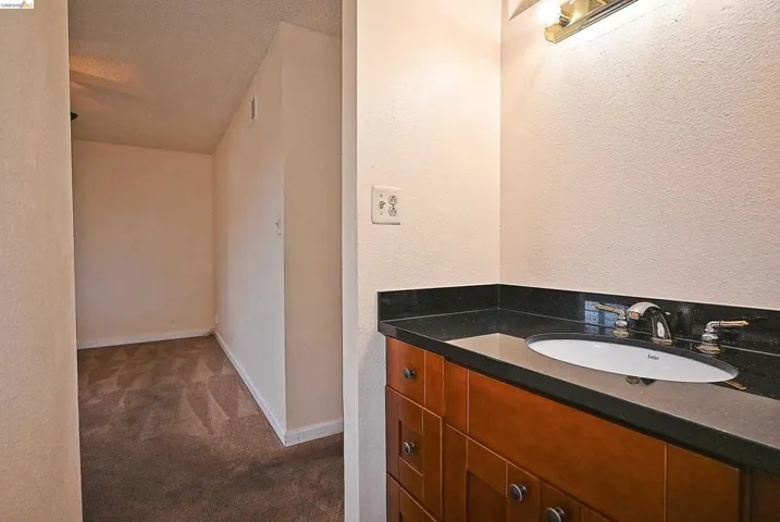 Bathroom featuring a textured wall, vanity, dark carpet, and a textured ceiling