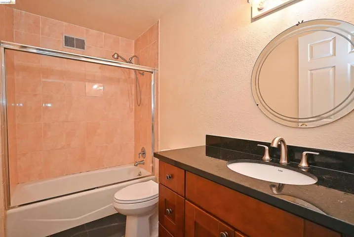 Full bath with a textured wall, vanity, bathing tub / shower combination, and dark tile patterned floors