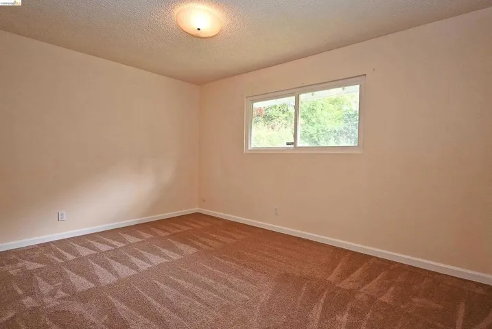 Carpeted empty room featuring baseboards and a textured ceiling