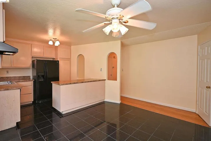 Kitchen with arched walkways, black fridge, light wood finish cabinetry, ceiling fan, and a textured ceiling