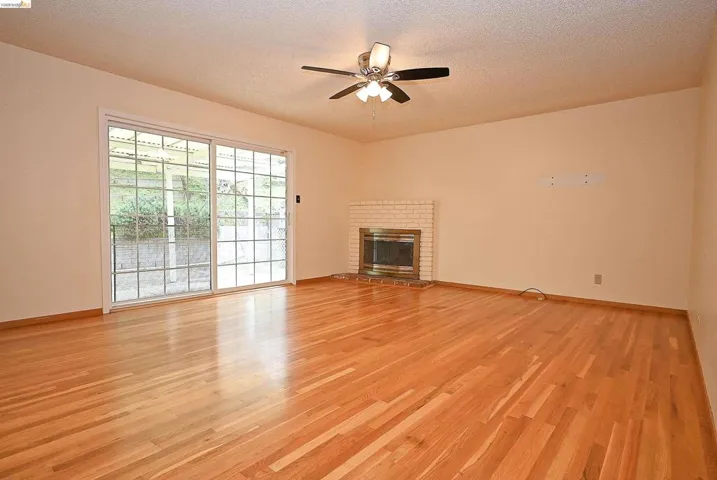 Unfurnished living room with light wood-style flooring, a textured ceiling, a ceiling fan, and a fireplace