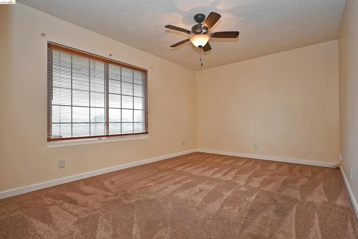 Carpeted spare room with ceiling fan and a textured ceiling