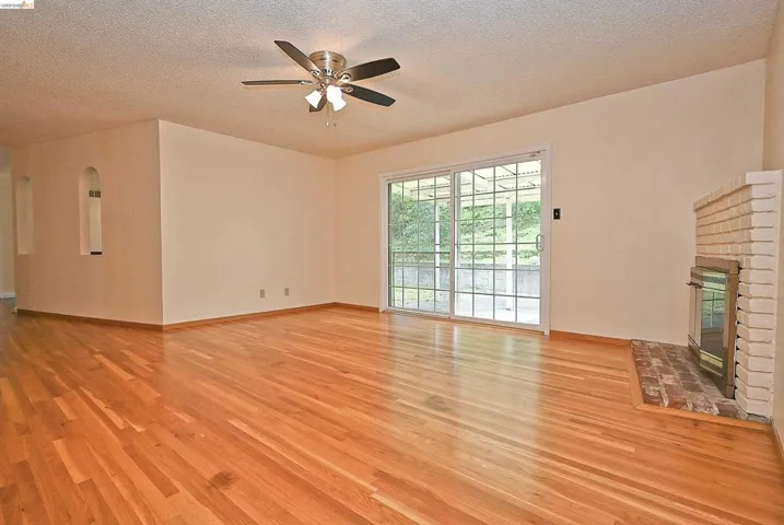 Unfurnished living room featuring a brick fireplace, light wood finished floors, a textured ceiling, and a ceiling fan