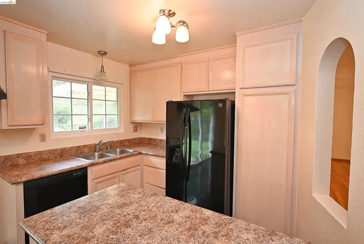 Kitchen featuring black appliances, pendant lighting, light wood finish cabinetry, and light countertops