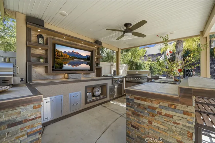 Outdoor kitchen with lighting, fan, BBQ, Griddle, outdoor TV, sink and fridge.