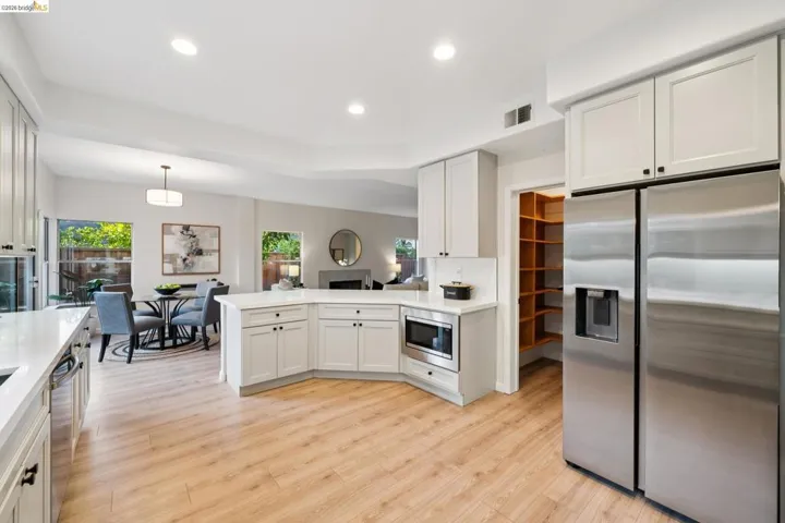 Kitchen with stainless steel appliances, a peninsula, white cabinetry, light wood-style floors, and hanging light fixtures