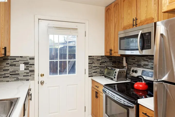 Kitchen with stainless steel appliances, wood finish cabinets, and light stone countertops
