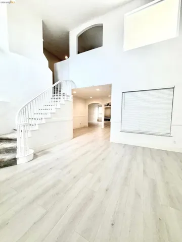 Unfurnished living room featuring a high ceiling, arched walkways, and light wood finished floors