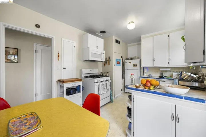 Kitchen with tile counters, light flooring, white cabinets, white appliances, and open shelves