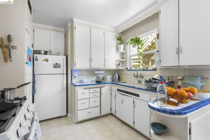 Kitchen with tile counters, open shelves, light floors, white appliances, and white cabinets