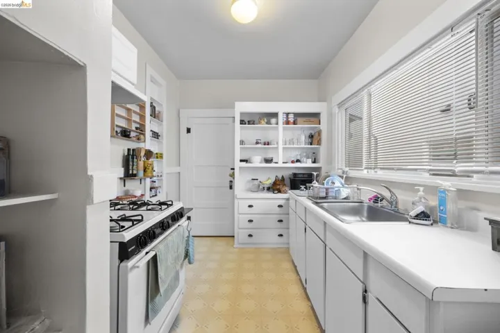 Kitchen featuring open shelves, gas range gas stove, light countertops, light flooring, and white cabinetry