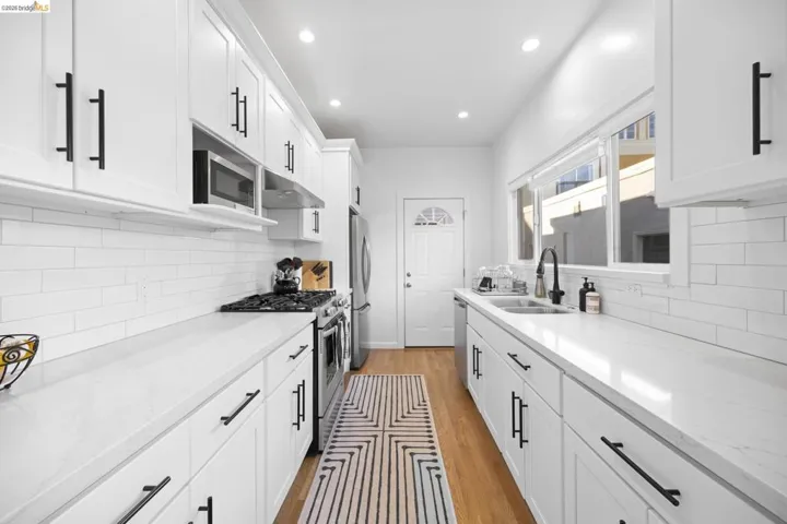 Kitchen featuring stainless steel appliances, white cabinets, light stone countertops, light wood-style flooring, and recessed lighting
