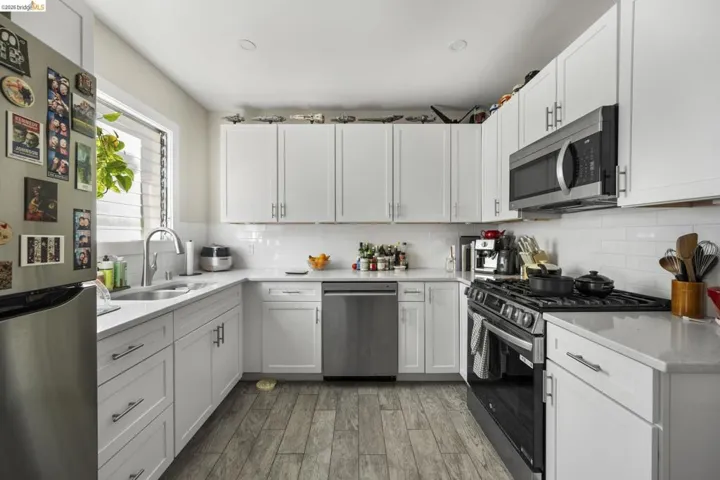Kitchen with stainless steel appliances, white cabinetry, light wood-style flooring, and light stone countertops