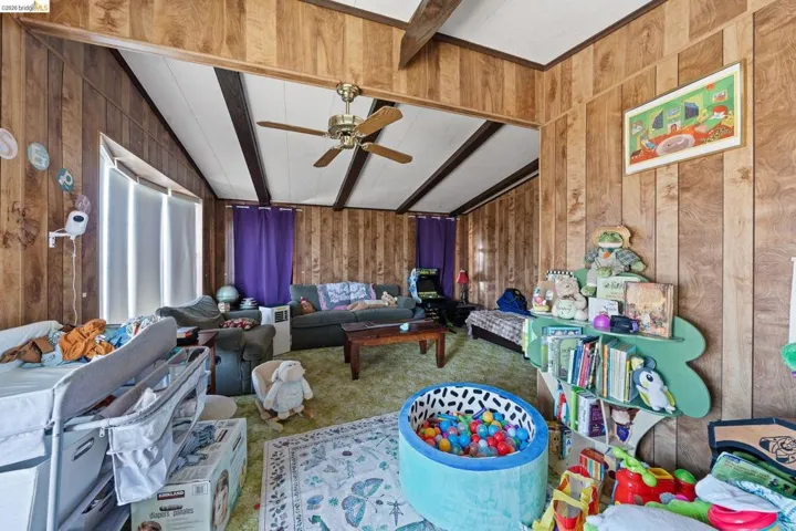 Carpeted living room featuring wood walls, lofted ceiling with beams, and a ceiling fan