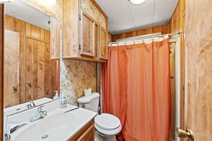 Full bathroom featuring vanity, wallpapered walls, a shower with shower curtain, and wooden walls