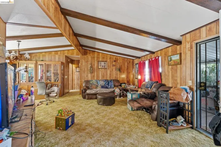 Living area featuring lofted ceiling with beams, carpet floors, plenty of natural light, wooden walls, and an office area