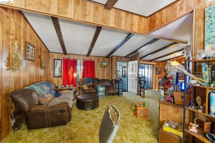 Living area featuring beamed ceiling, wood walls, and carpet flooring