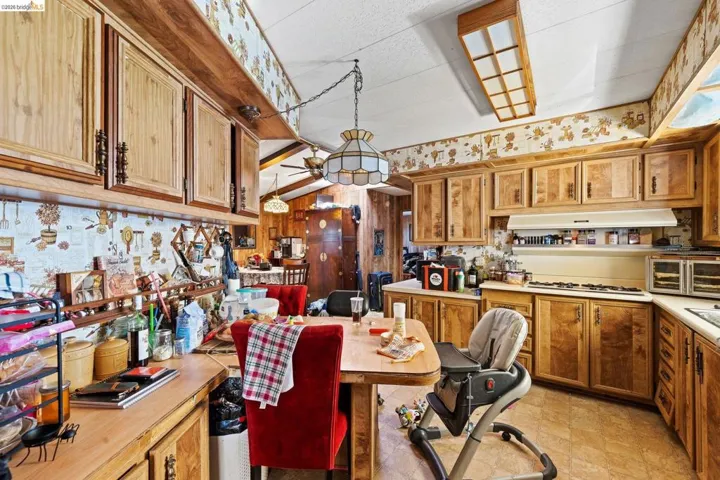 Kitchen featuring wood finish cabinetry, light countertops, wallpapered walls, white gas cooktop, and pendant lighting