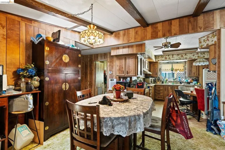 Dining room with wood walls, a textured ceiling, hanging lights, beam ceiling, and a ceiling fan