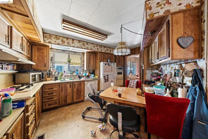Kitchen with white appliances, wood finish cabinets, wallpapered walls, light countertops, and a textured ceiling