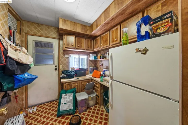 Kitchen with freestanding refrigerator, wood finish cabinetry, light countertops, and light flooring