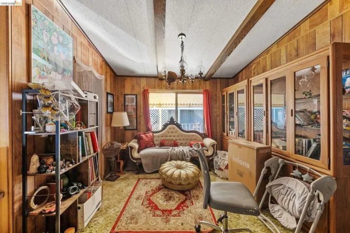 Sitting room with hanging lights, wood walls, a textured ceiling, and light colored carpet