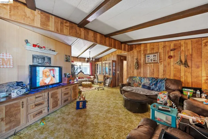 Living room featuring wooden walls, suspended lighting, carpet flooring, and lofted ceiling with beams