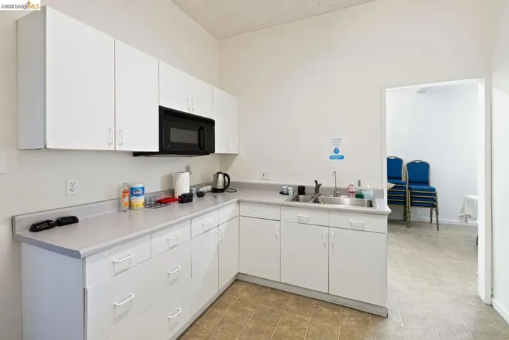 Kitchen with light countertops, white cabinetry, black microwave, and a high ceiling