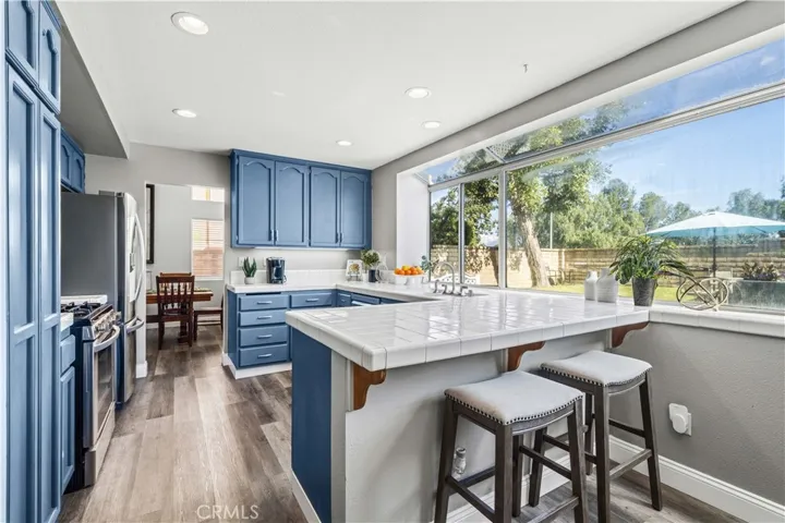The kitchen features blue cabinetry, tile countertops, and a large bay window that looks out to the yard.