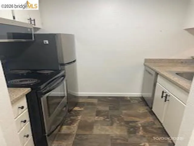 Kitchen with electric range, stone finish floors, white cabinets, and stainless steel dishwasher