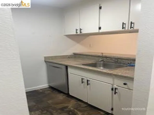 Kitchen with white cabinets, stainless steel dishwasher, and a textured wall