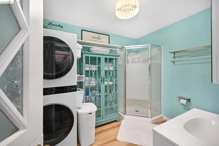Full bath featuring vanity, a stall shower, stacked washer and clothes dryer, and wood finished floors