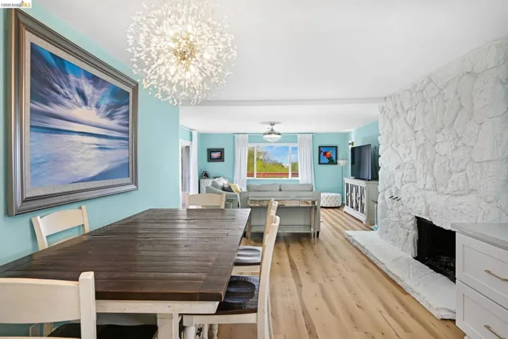 Dining room with suspended lighting, light wood-type flooring, and a stone fireplace