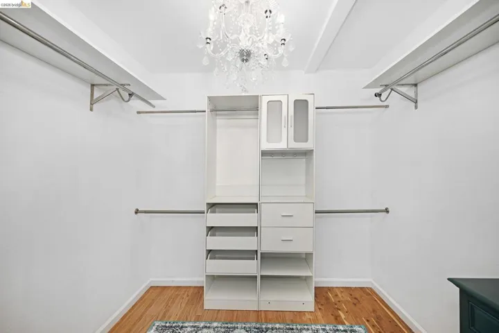 Walk in closet with hanging lights and light wood-style flooring