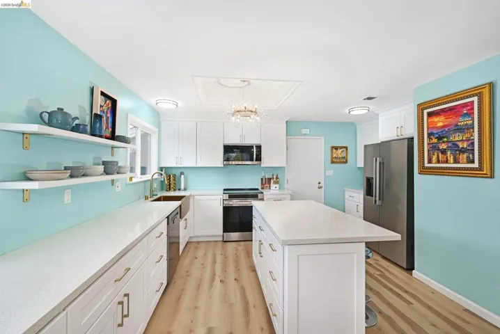 Kitchen with open shelves, stainless steel appliances, white cabinets, light stone counters, and light wood-style flooring